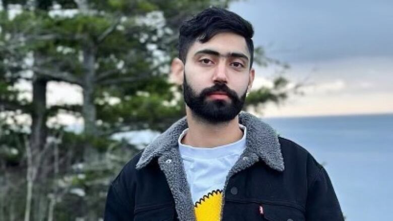 A South Asian man smiles while in a waterfront environment.