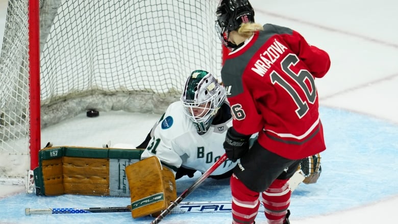 A women's hockey player scores a game-winning goal while the opposing goalie lays on the ice.