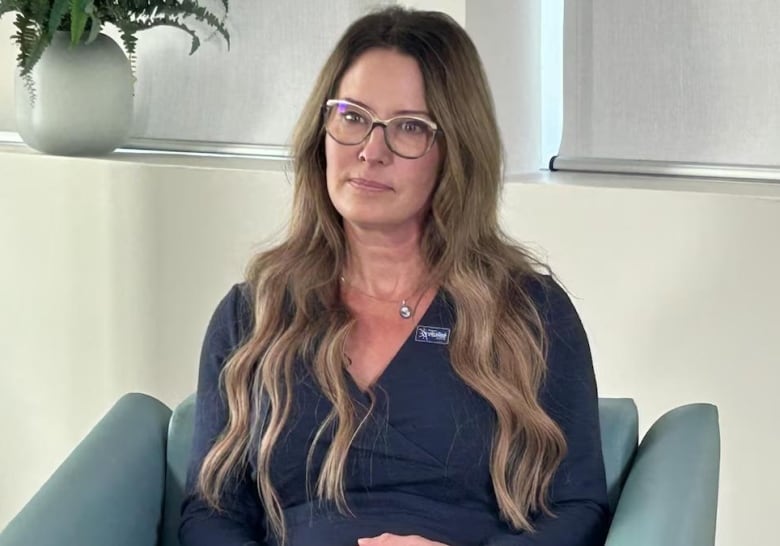 An unsmiling woman with long, wavy hair and glasses.