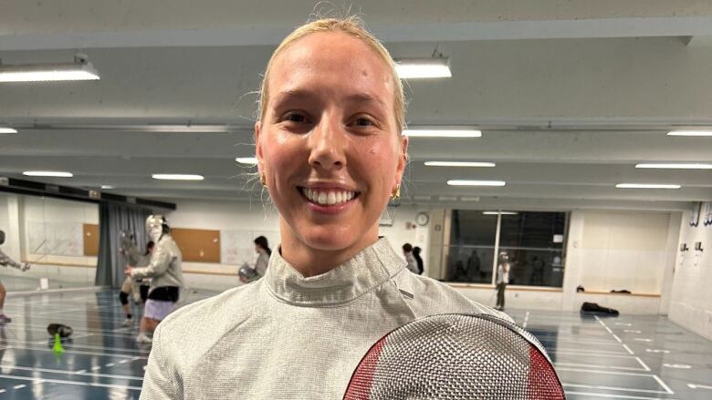 An athlete smiling while dressed in fencing attire. 