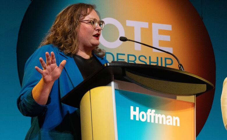 A woman gestures behind a debate lectern.