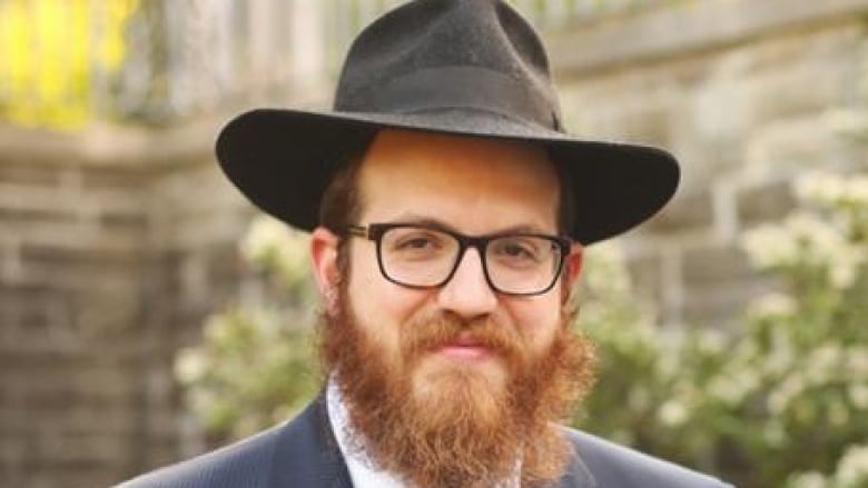 A rabbi with a beard smiles to camera