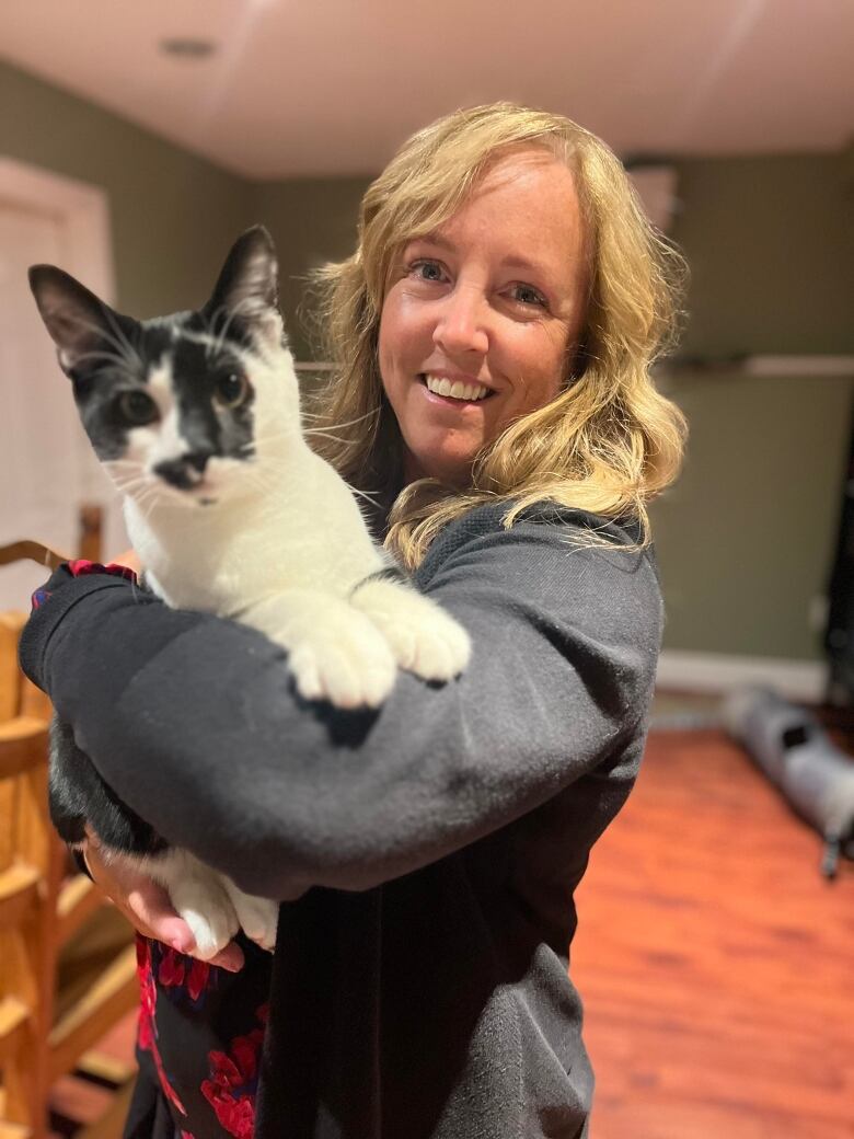 A woman with blonde hair holds a cat in her arms.