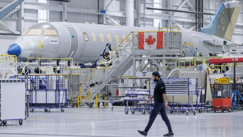 Man walks by a jet being assembled in a Bombardier plant.