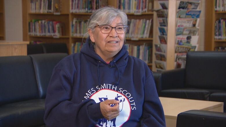 A women, who is wearing a darn hooded sweater sits in a chair to do an interview.