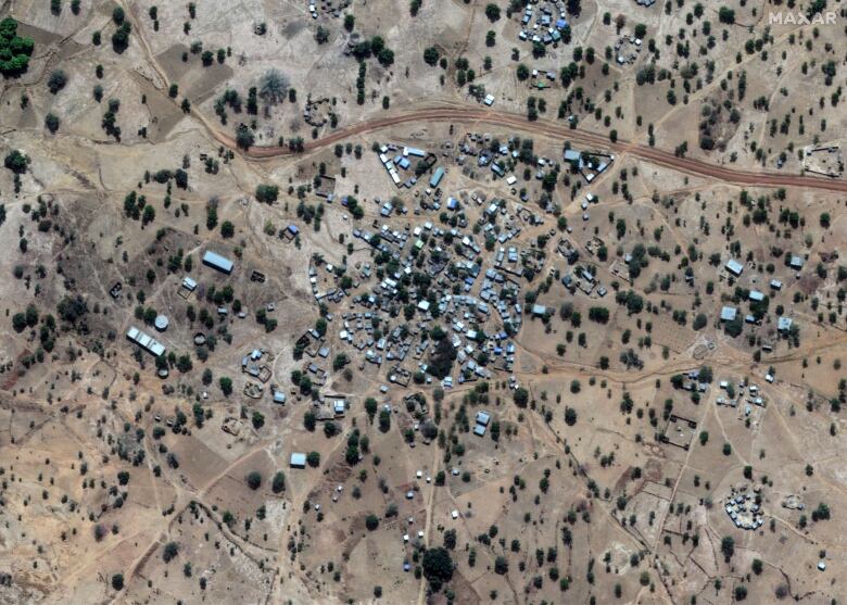 A small village pictured from above with a cluster of houses and buildings in a sandy terrain dotted by trees.