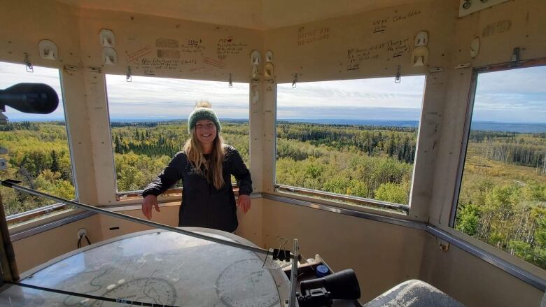 A woman standing in a tower overlooking trees smiles.