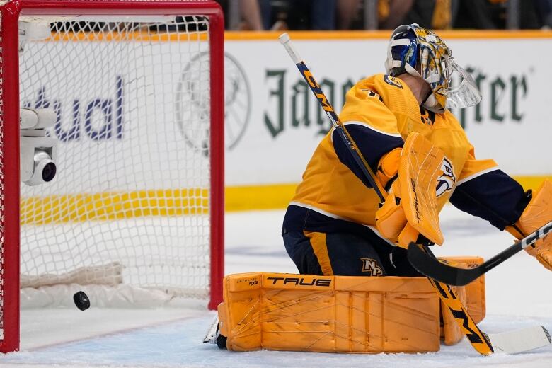 A goalie lets a puck into a hockey net.