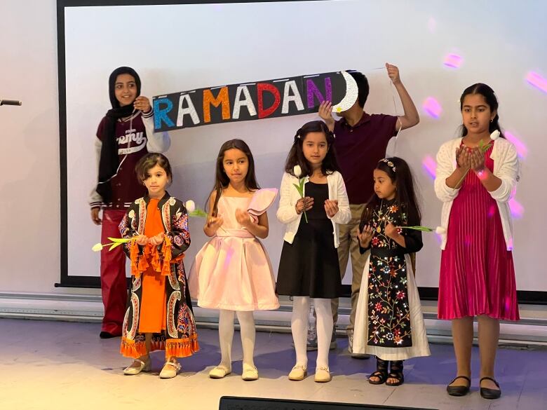 A number of children hold flowers as they perform a dance number.