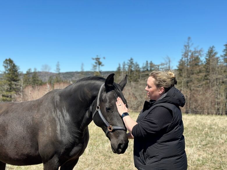 A woman pets a black mare on the head.