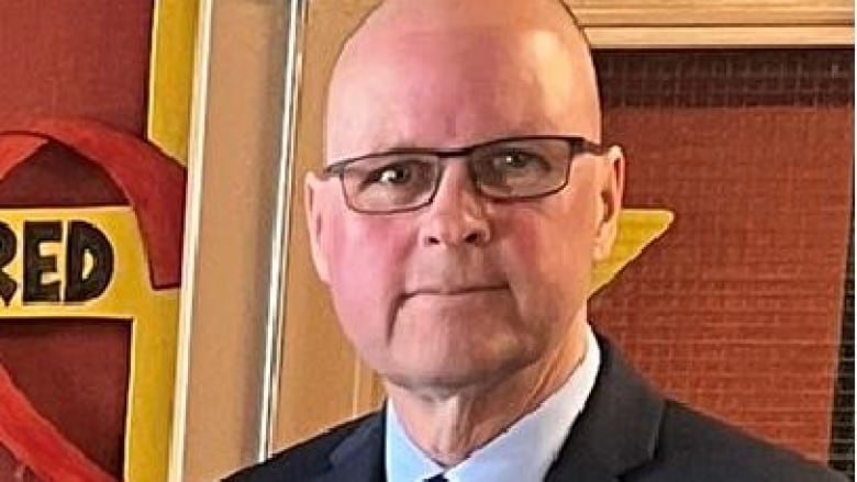 a bald white man in glasses poses for a picture