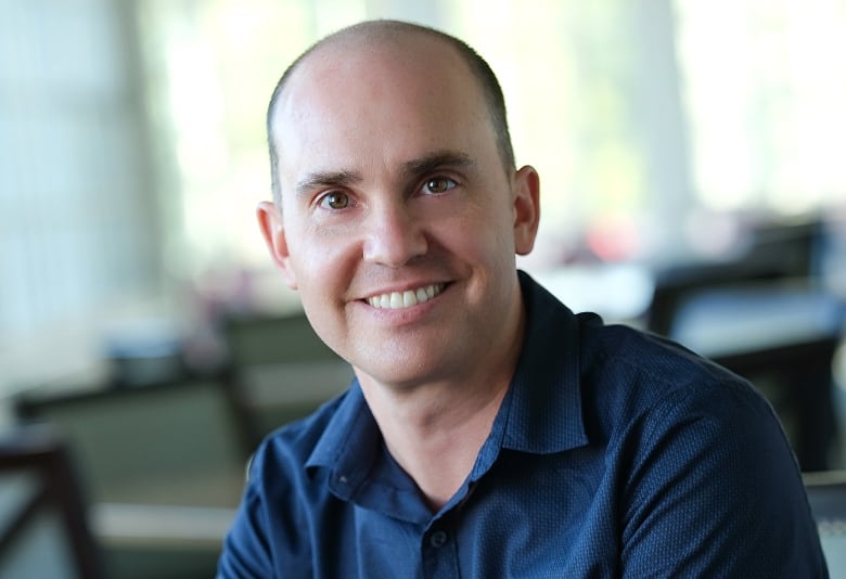 Man in a blue shirt smiling directly at the camera. 