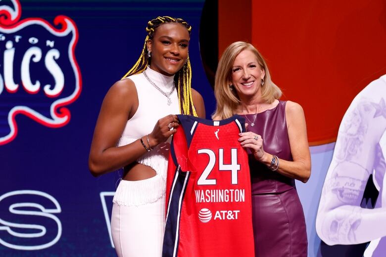 A woman is presented with a basketball jersey by another woman.