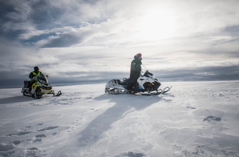 Two men on snowmobiles outside in the snow. 