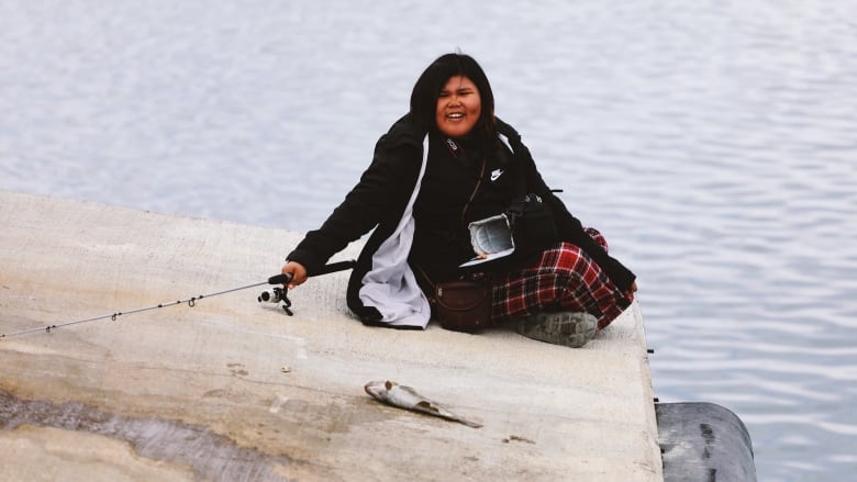 A young girl holds a fishing pole on a dock. 