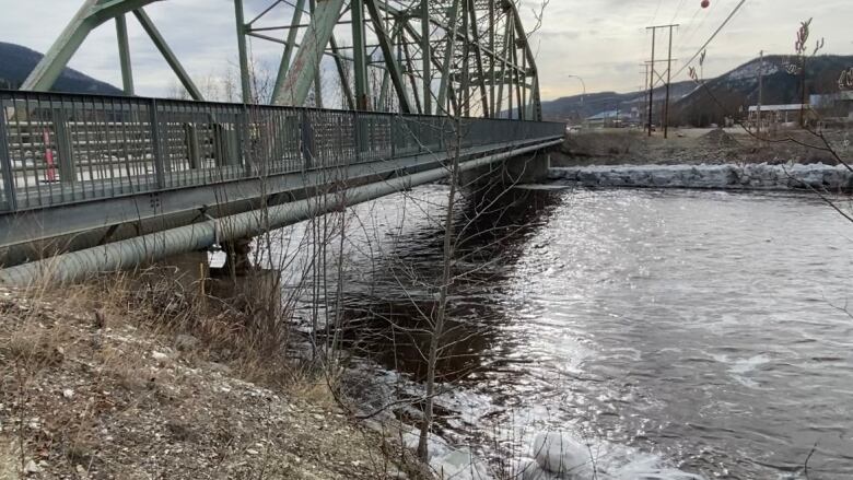 A highway bridge is seen over a river with snow and ice on its banks.