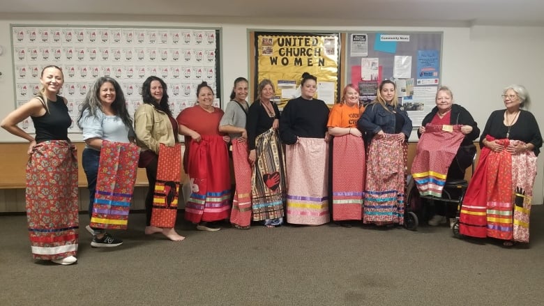 A group of women stand in a row, each holding bright red ribbon skirts.