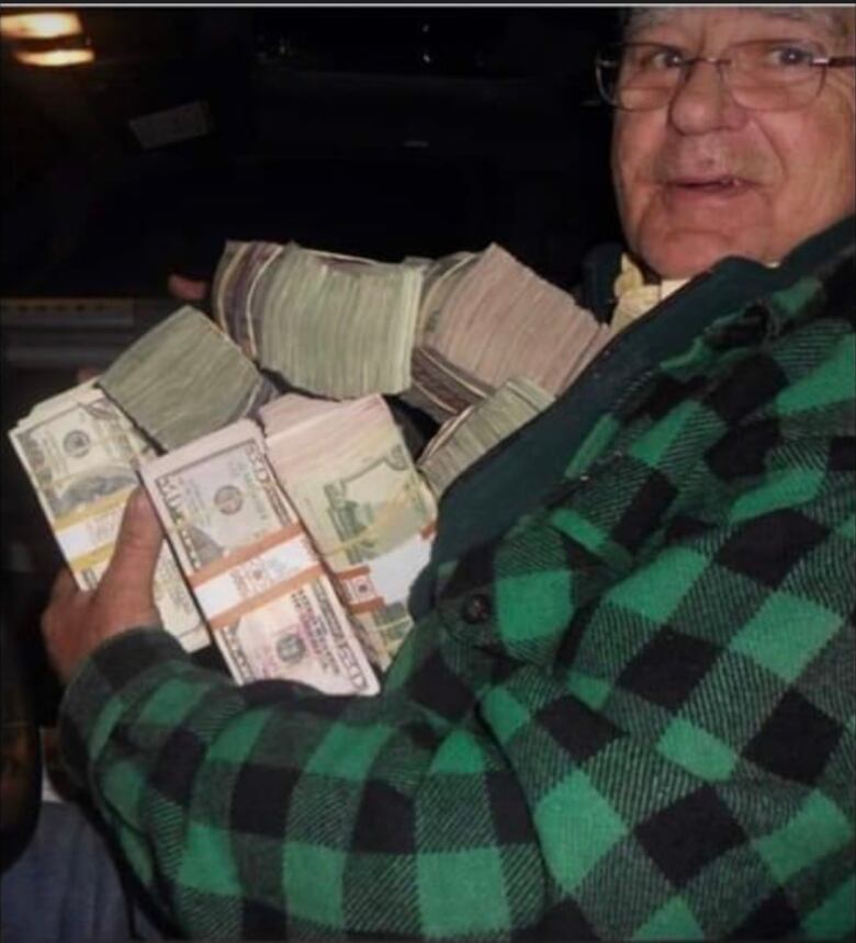 Man poses with an armful of stacks of cash