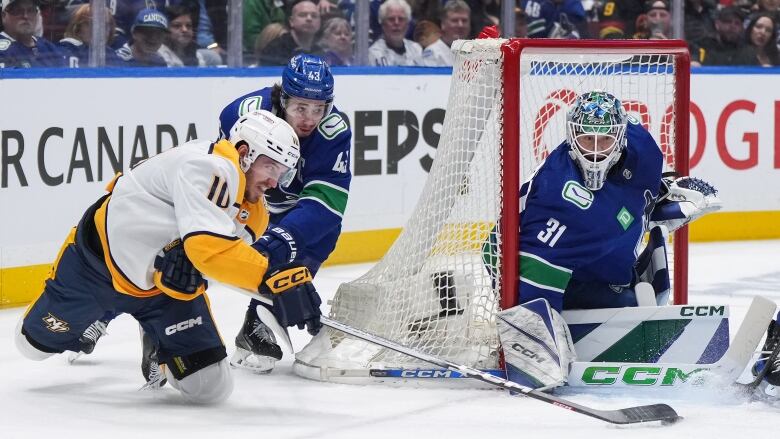 A male hockey player in a white and gold jersey is on the ice on his knees attempting to score on a goalie.