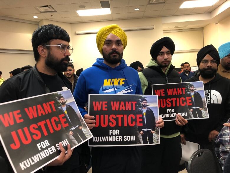 A group of SOuth Asian men hold up signs saying 'We Want Justice for Kulwinder Sohi'.