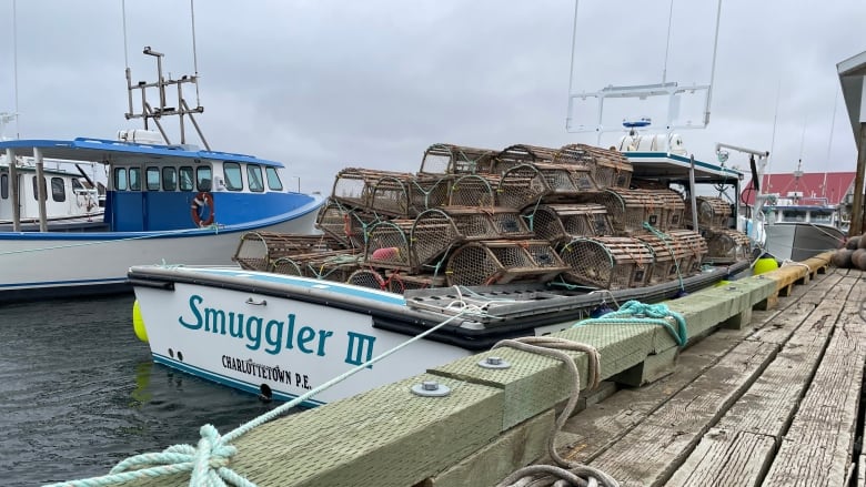 A white lobster boat tied to a wharf and loaded with lobster traps in the back.