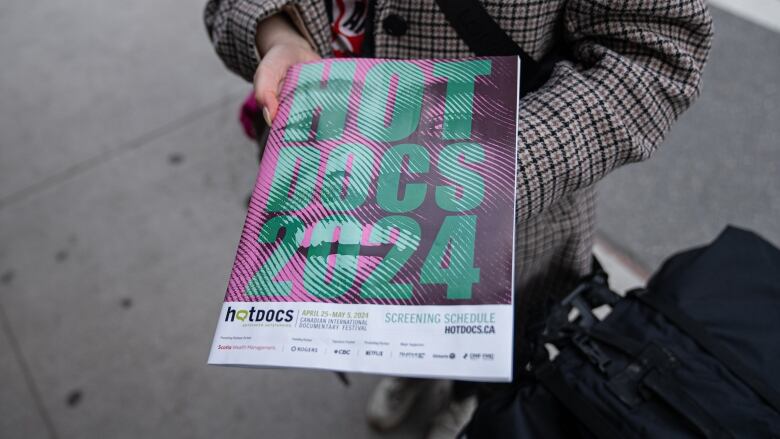 A person holds a festival screening schedule. On the cover are the words 'Hot Docs 2024.'