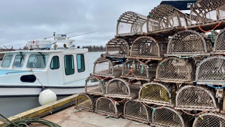 Lobster traps stacked on a wharf next to a tied up boat.