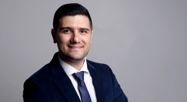 Hamed Vatankhah smiles at the camera, wearing a navy blue suit and tie.