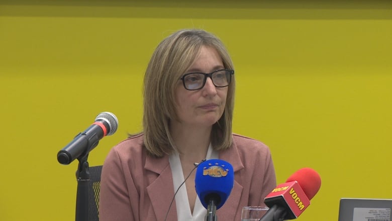 A woman wearing a pink blazer sits in front of a large yellow wall.