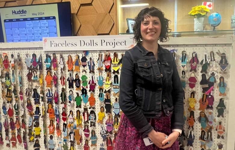 A woman is pictured smiling as she stands in front of a display of dolls.