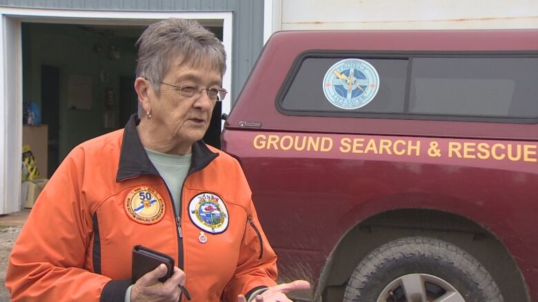 Woman in orange coat stands in front of a search and rescue truck 