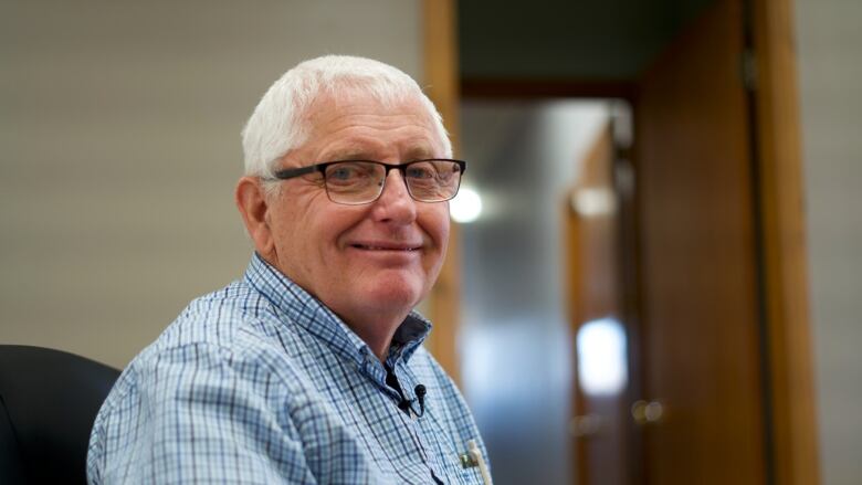 A man with short grey hair and glasses smiles while sitting in an office.