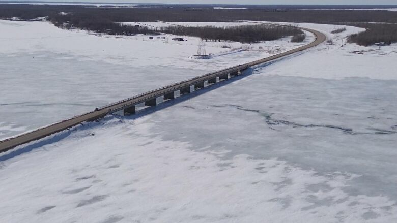 An aerial shot shows cracks in a frozen lake and a bridge passing over the ice.