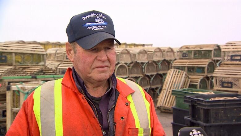 Older man with hat and reflective jacket stands on dock near water.