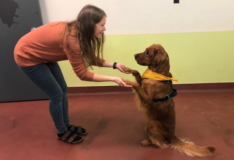 A woman is holding the paws of a dog, looking happy.