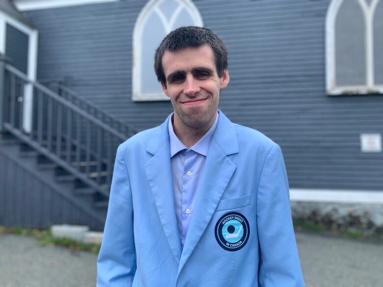 A smiling man wearing a powder blue blazer with the retro Hockey Night in Canada logo on the right pocket.