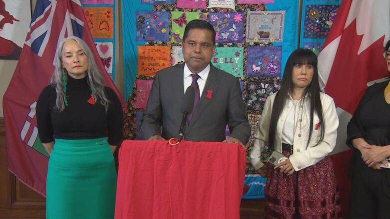 A man stands at a podium, flanked by two women.