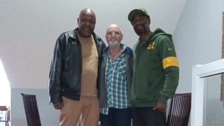 Three men stand together and smile for a photo.