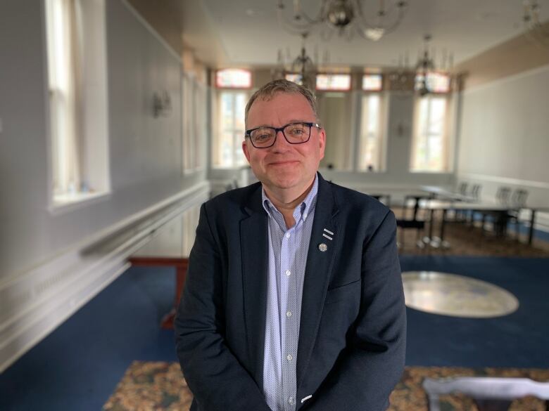 A man with glasses stands in a room.