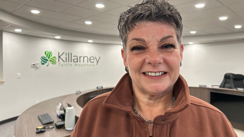 A smiling woman stands near a semi-circular reception desk. The wall beyond says 