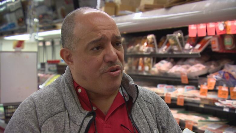 A man with a grey sweater stands in a grocery store.