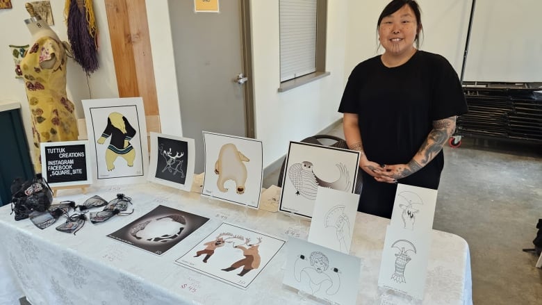 Indigenous woman with cultural tattoos on her face standing next to a table with her art on it.