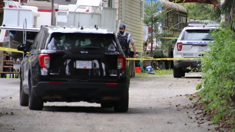 A police officer stands behind crime tape on a rural property.