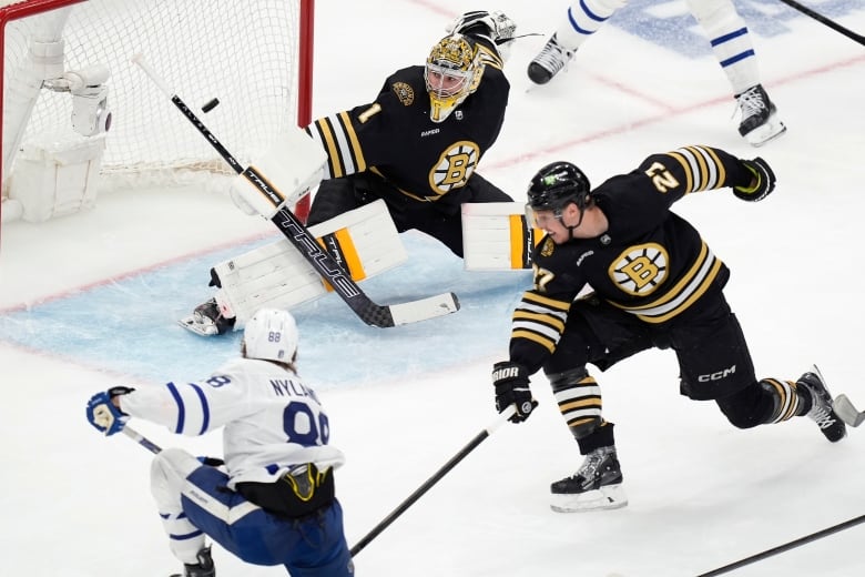 A hockey player shoots a puck going past a goalie.