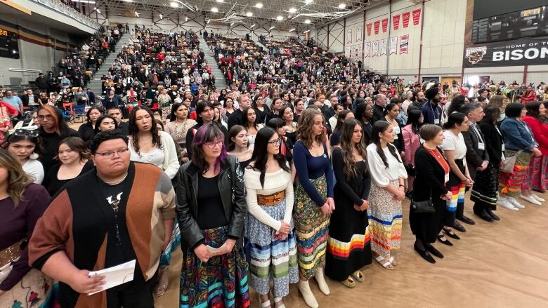 A crowd stands in a gymnasium.