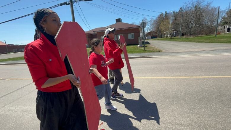 Four people walk through a street, with two people holding wooden cutouts of red dresses.