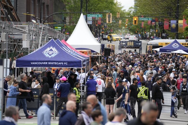 A large group of soccer fans are seen milling around in a street with various tents set up.