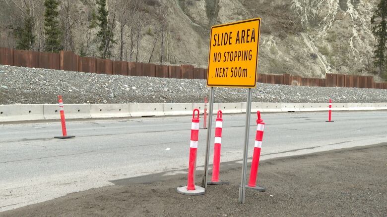 Pylons are seen on a road near a sign warning of potential slides.