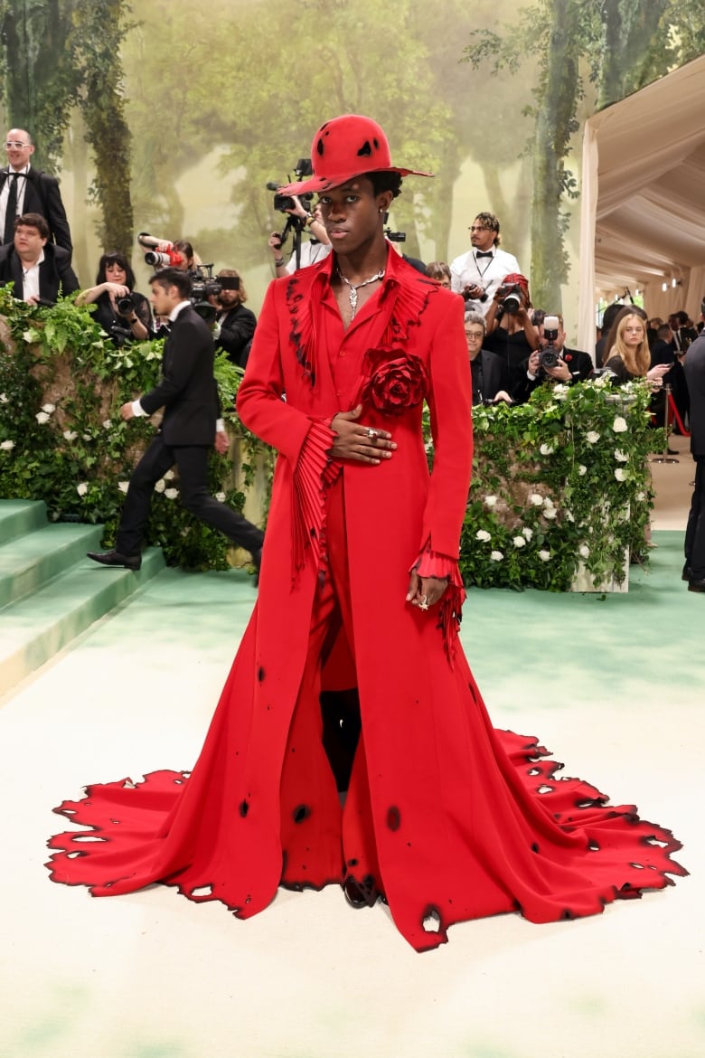 Wisdom Kaye wearing an all-red suit and hat with a jacket that has a rose on the lapel and a long train. 