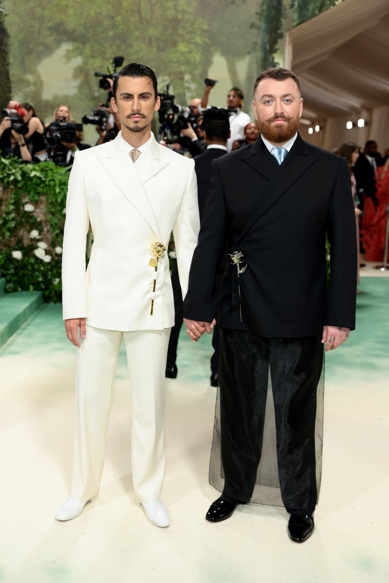 Christian Cowan and Sam Smith on the Met Gala red carpet. Cowan is wearing a cream double-breasted tuxedo and Smith is wearing a black double-breasted tuxedo. 